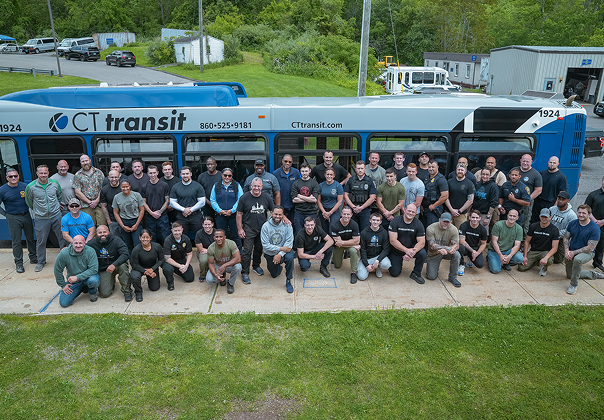 Large group of CTtransit employees posing together in front of a CTtransit bus outdoors.